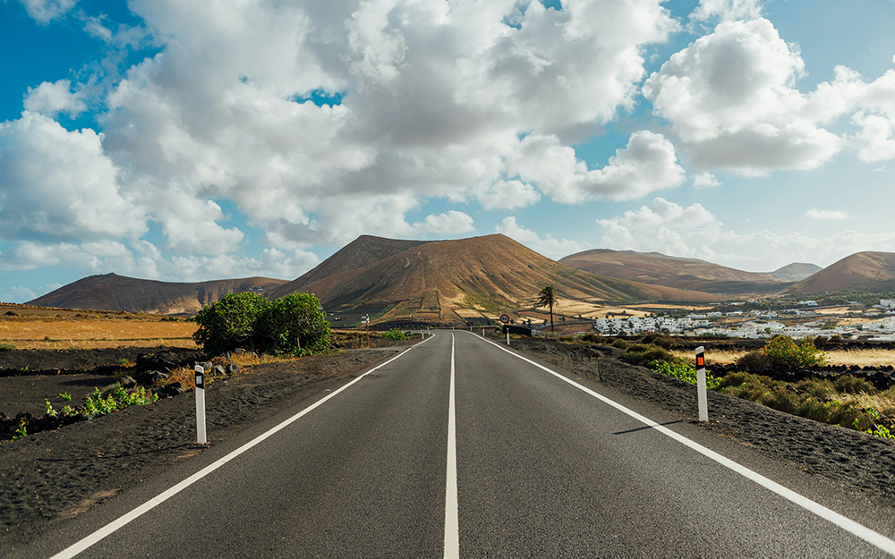 escapadas de lujo baratas: Lanzarote. Imagen de una carretera con paisaje volcánico de fondo